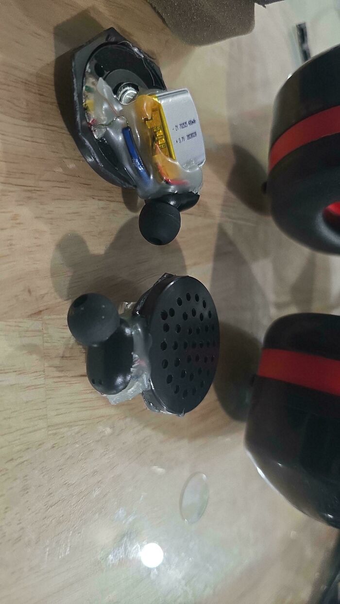 Disassembled wireless earbuds showing internal battery and speaker components on a wooden surface, tech support fail example.