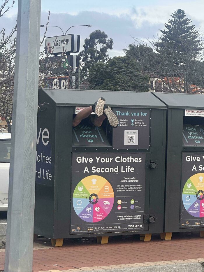 A person with their legs sticking out of a clothing donation bin, possibly looking for items during dumpster diving.