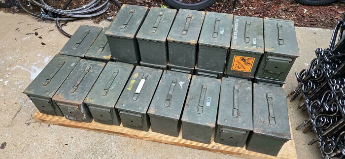 Large collection of military-style green ammo boxes stacked neatly on a wooden pallet, found during dumpster diving.