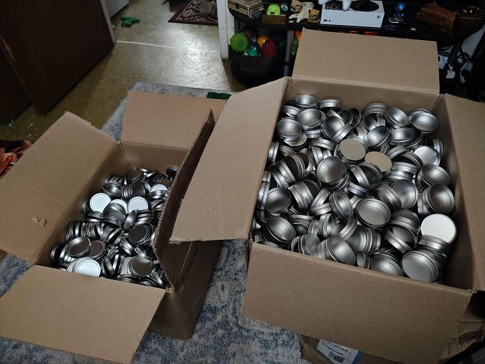 Two large cardboard boxes overflowing with numerous small, round metal containers, excellent finds from dumpster diving.