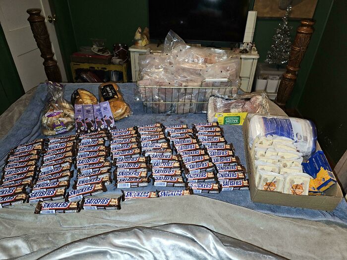 A large haul of Snickers candy bars, packaged meats, and other items neatly laid out on a bed, showcasing successful dumpster diving.