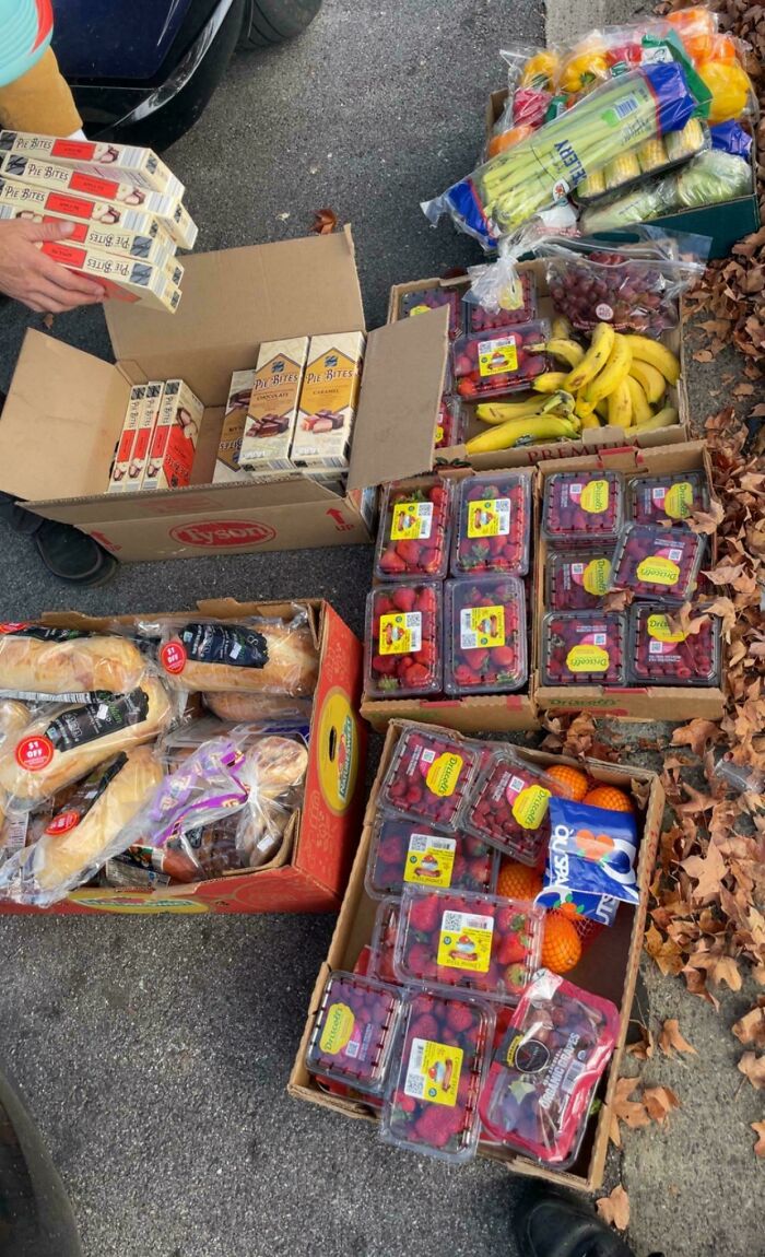 Various boxes overflowing with fresh fruits like strawberries, bananas, and grapes, along with bread and packaged goods from dumpster diving.