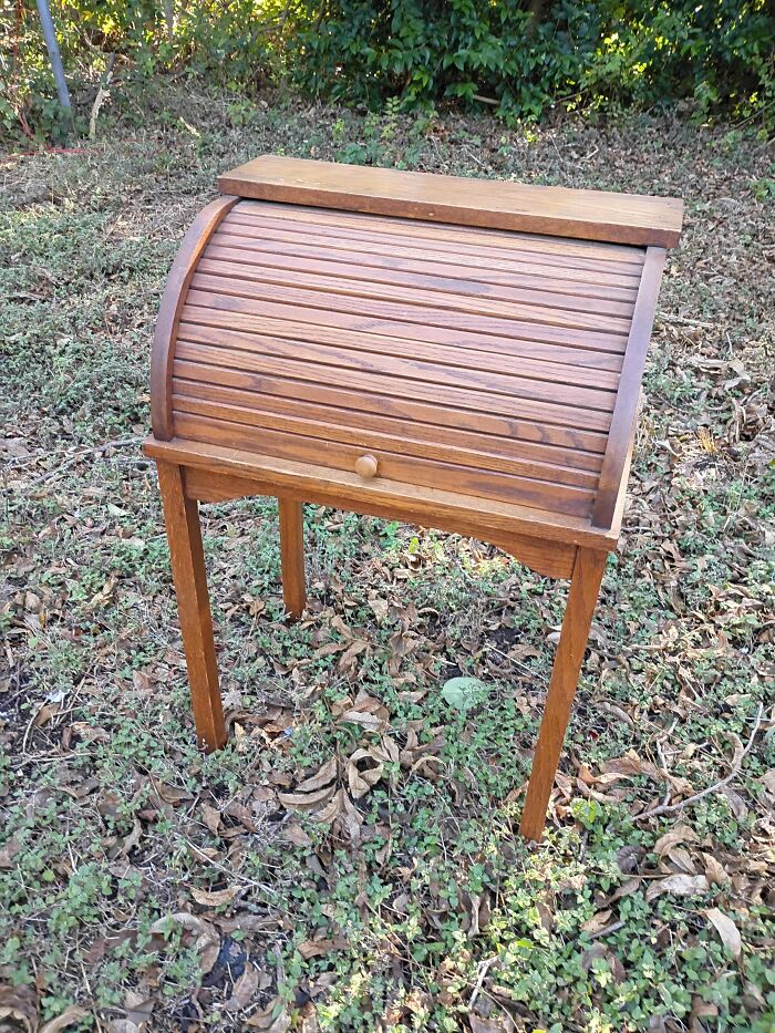 A vintage wooden roll-top desk standing outdoors, a fortunate find from dumpster diving.