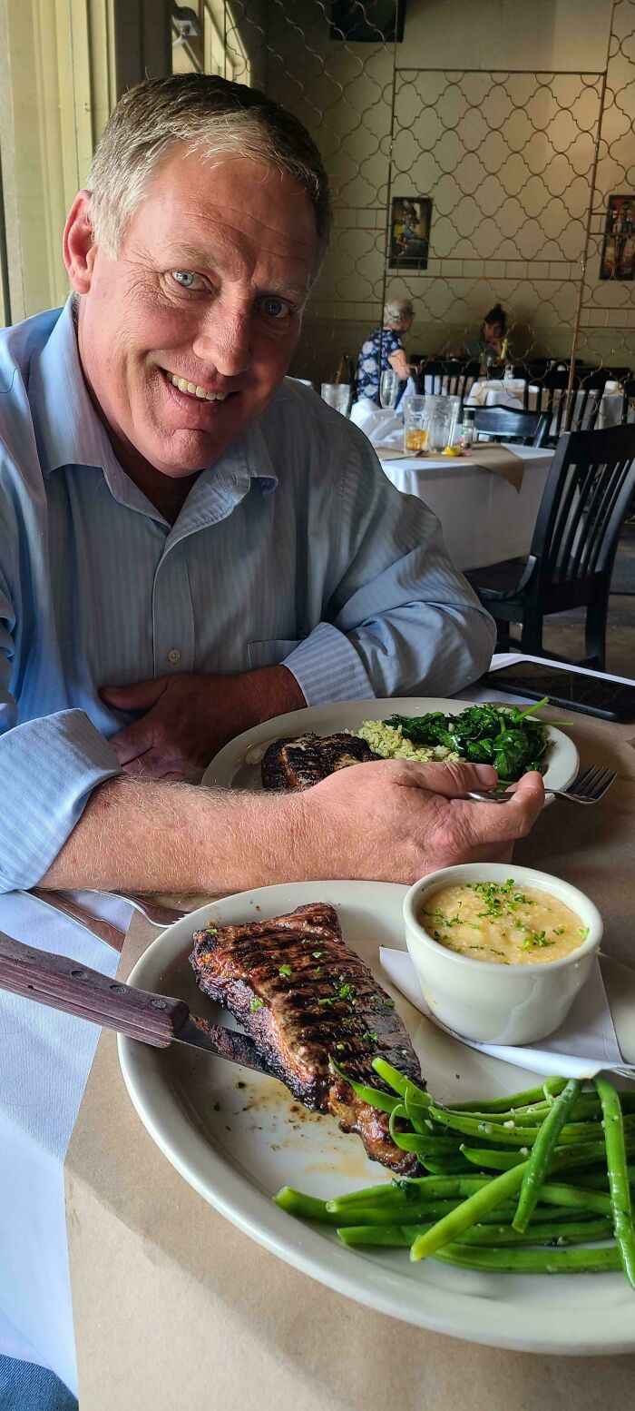 A smiling man enjoying a meal of steak, green beans, and mashed potatoes, a lucky dumpster diving discovery.