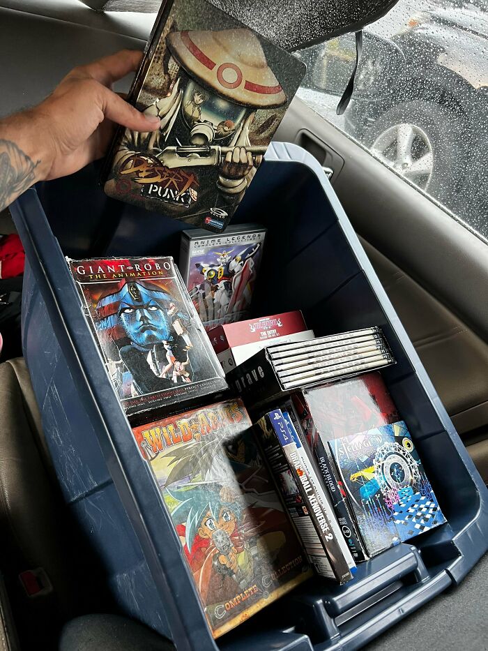 A bin full of anime DVDs and video games, showcasing incredible luck from dumpster diving, being placed into a car.