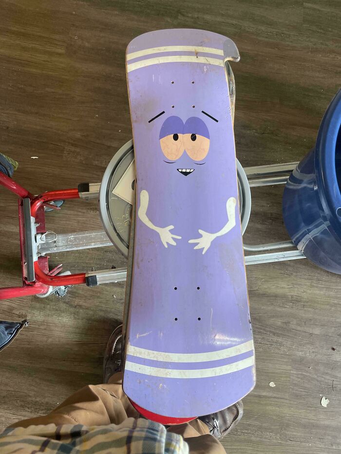 A South Park themed skateboard, a lucky find from dumpster diving, stands upright against a wooden floor.