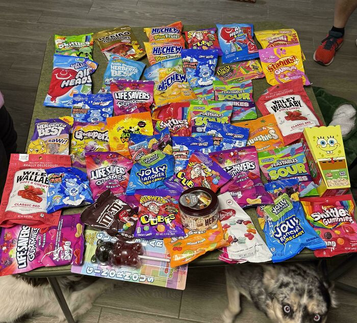 A large haul of various candy bags and boxes spread across a table, a sweet treasure found through dumpster diving.