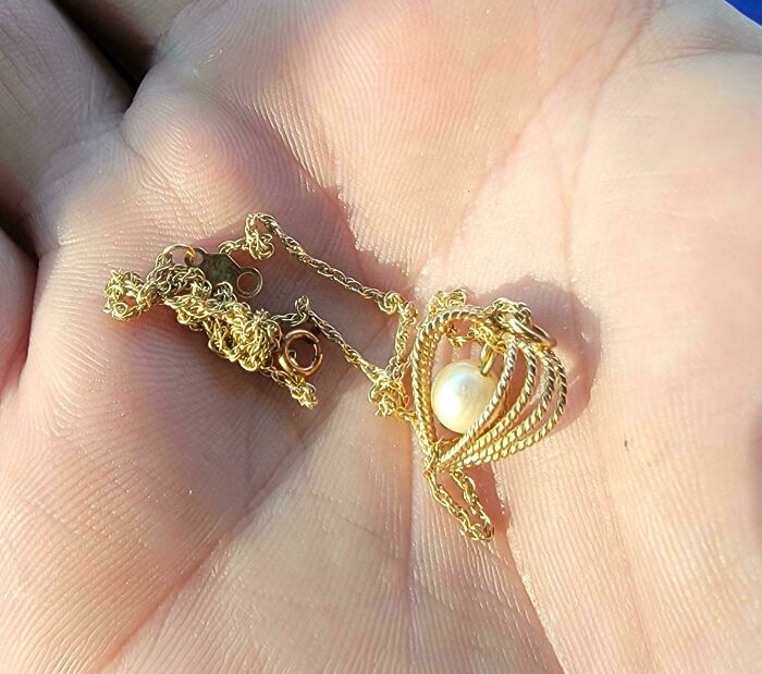 A delicate gold necklace with a pearl pendant resting in the palm of a hand, a valuable dumpster diving find.