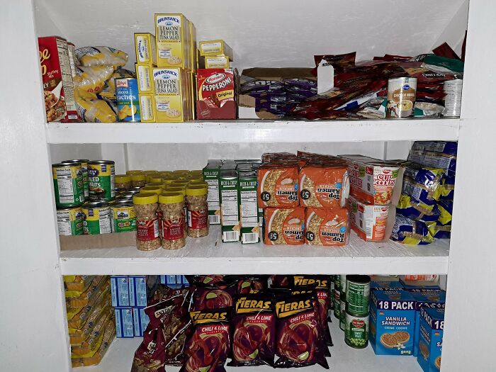 Shelves stocked with numerous boxes of ramen, canned goods, and snacks, all from dumpster diving.