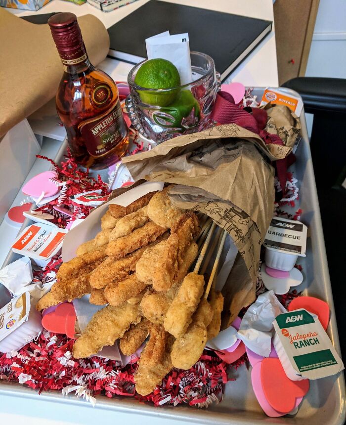 Valentine’s Day gifts tray with fried snacks on skewers, dipping sauces, mini liquor bottle, and festive heart decorations.