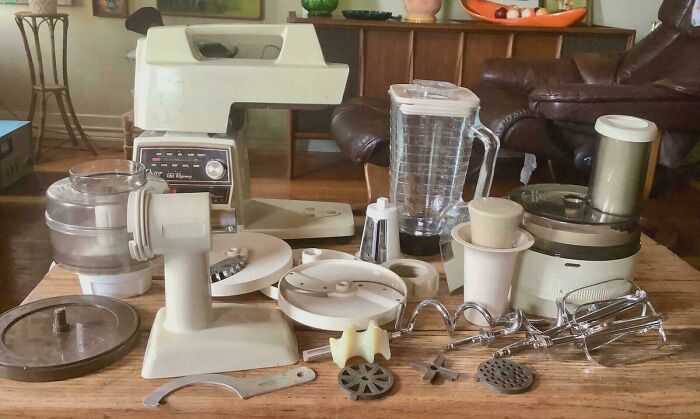A vintage KitchenAid mixer with numerous attachments spread on a wooden table, showcasing a Buy It For Life purchase.