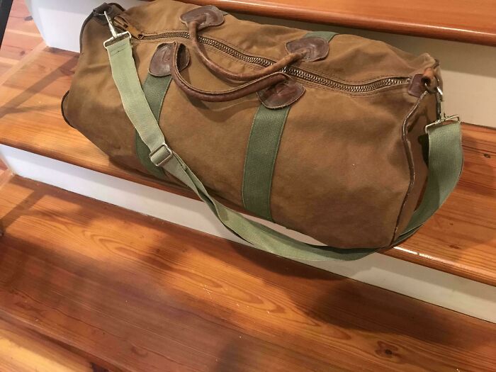 A well-worn brown canvas duffel bag with leather accents and a green strap, showcasing a true Buy It For Life purchase.