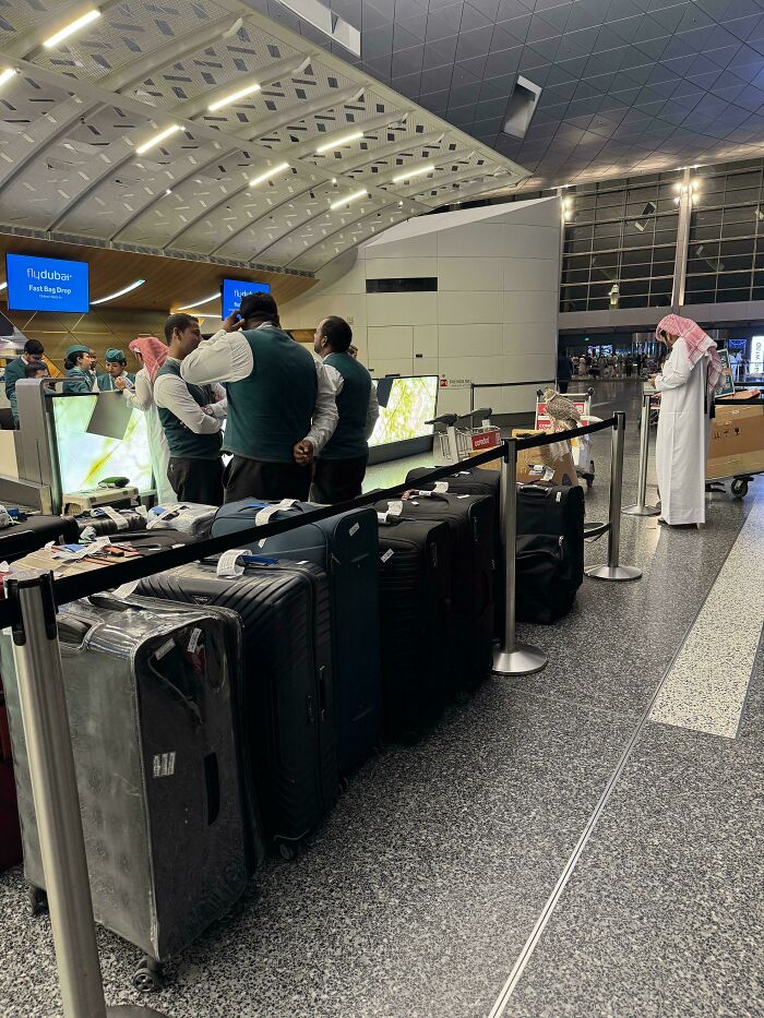 A line of suitcases at an airport check-in, with staff and a man in traditional attire, showcasing mildly interesting pictures.