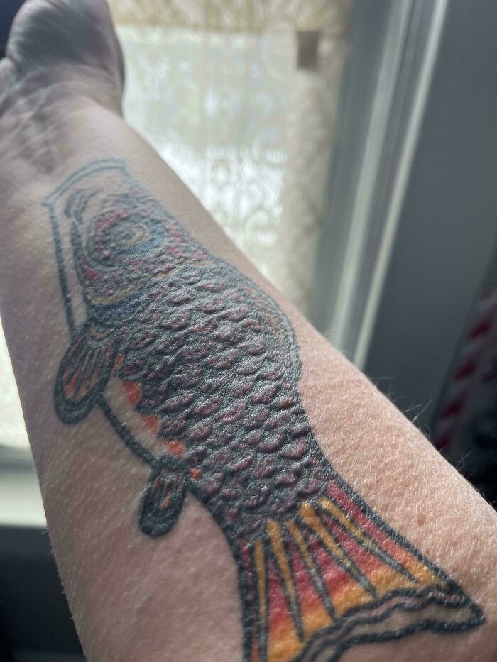 An arm with a fish tattoo, its scales raised, a truly interesting picture.