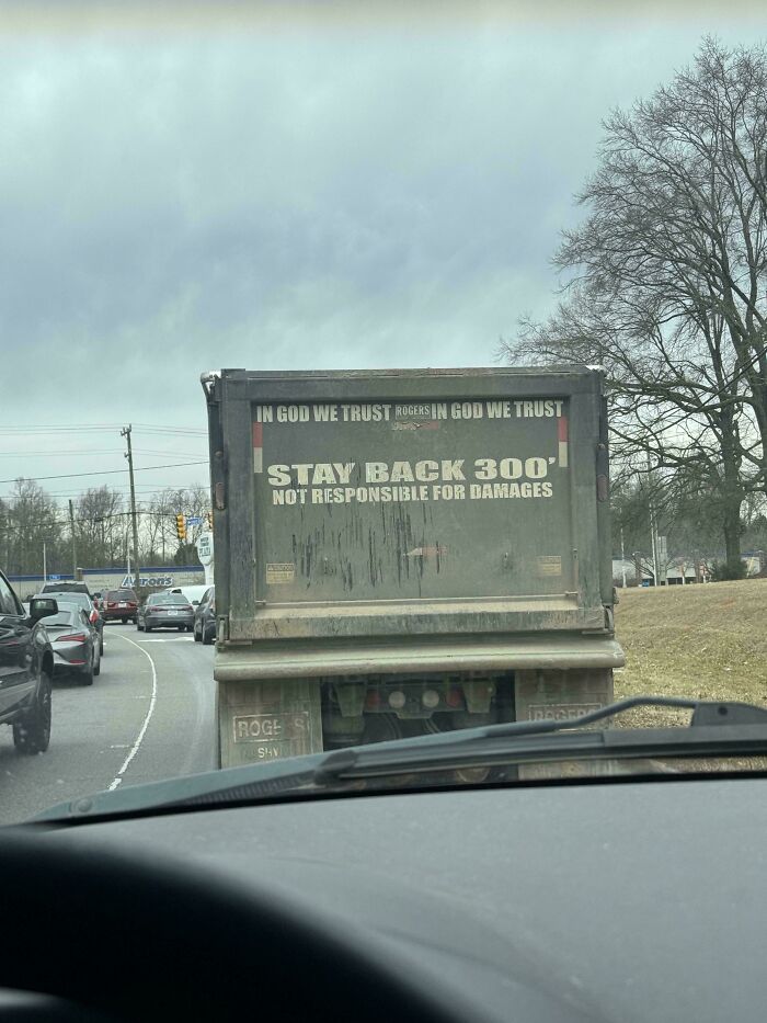 The back of a dirty dump truck with a warning sign, a mildly interesting picture seen from a car.