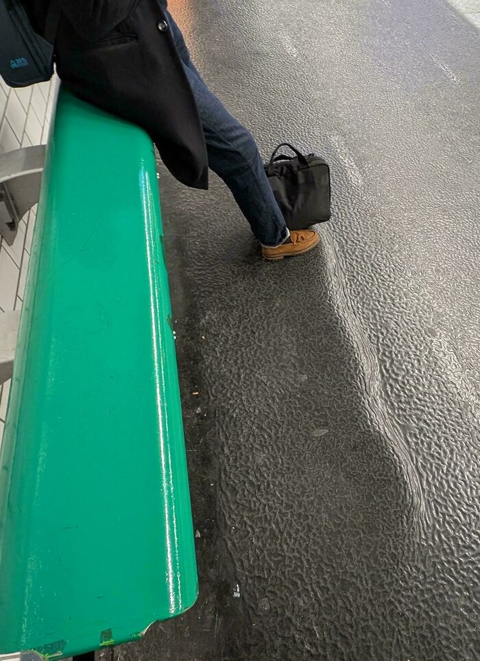 A person sits on a green bench with a black bag, showcasing a mildly interesting picture of urban textures.
