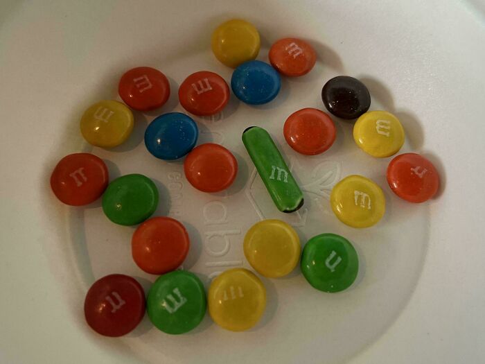 A pile of colorful M&Ms, with one green M&M standing upright, creating a mildly interesting picture.