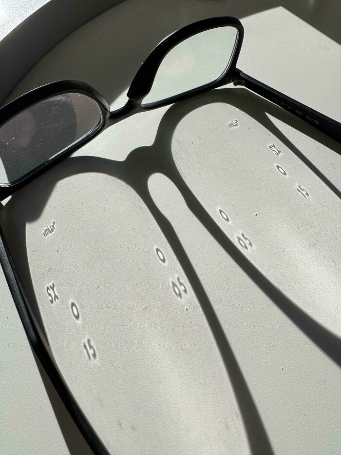 Black-framed glasses casting shadows that project numbers and letters onto a light surface, a mildly interesting picture.