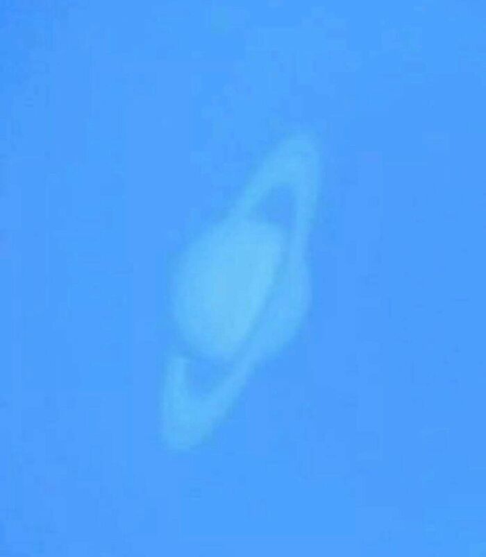 Faint cloud formation resembling a planet with rings against a clear blue sky during devil sunrise.