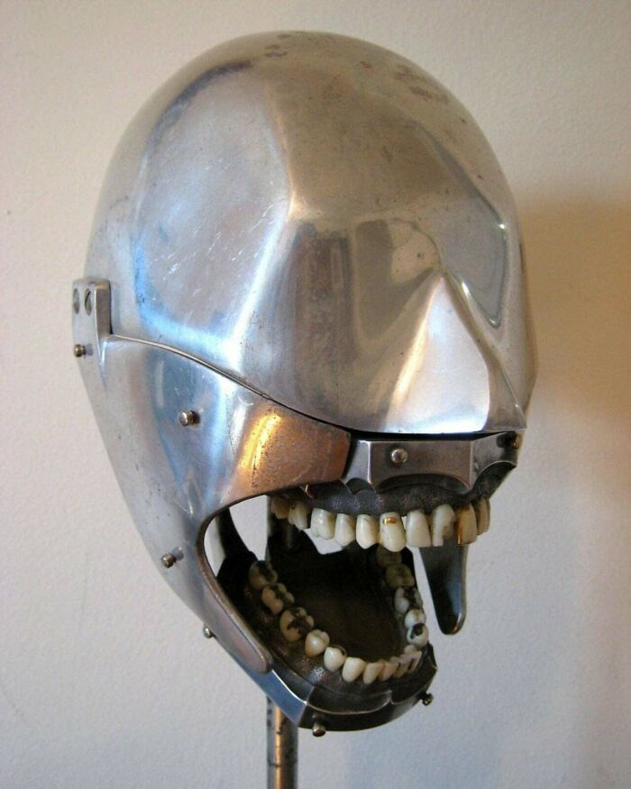 Metal helmet with realistic human teeth in an open mouth design, resembling a devil sunrise inspired artistic creation.
