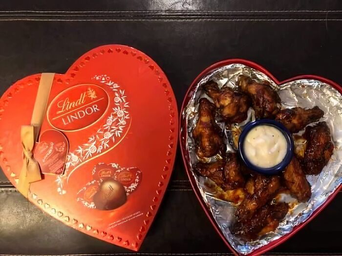 Heart-shaped box of chocolates next to heart-shaped container of chicken wings with dipping sauce funny Valentine’s Day gifts.