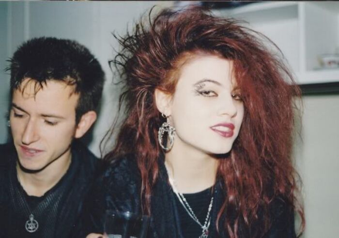 A young woman with iconic 80s hairdos featuring big, voluminous teased hair and bold makeup, next to a man.