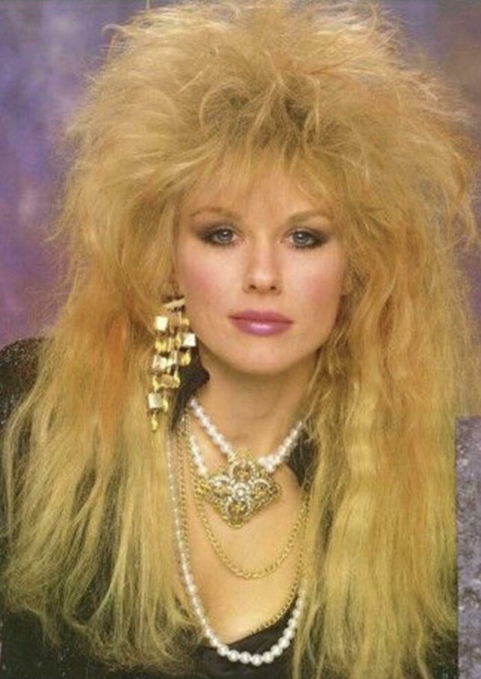 Woman with iconic 80s hairdo featuring big, teased blonde hair and bold accessories typical of 80s hairdos.