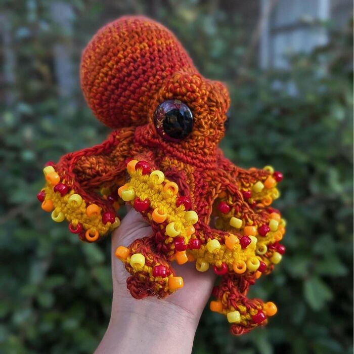 A vibrant crocheted octopus, orange and yellow with beaded tentacles, held in a hand. Awesome crocheted craft.