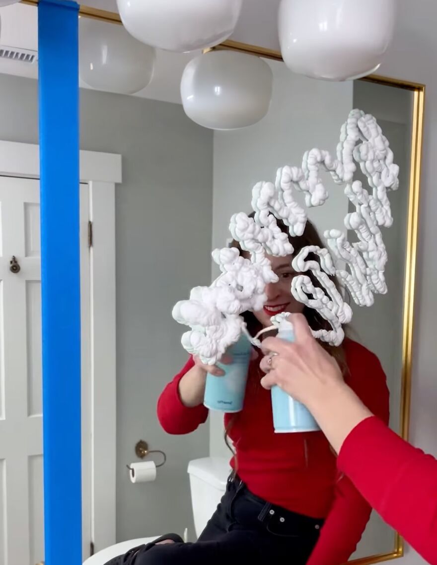 Woman using shaving cream on a mirror as a genius hack to prevent fog with everyday items in a modern bathroom.