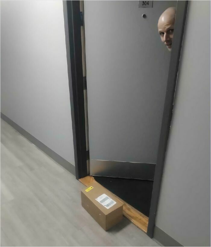 Delivery confirmation pic showing a package left at an apartment door with a driver peeking out from behind the door.