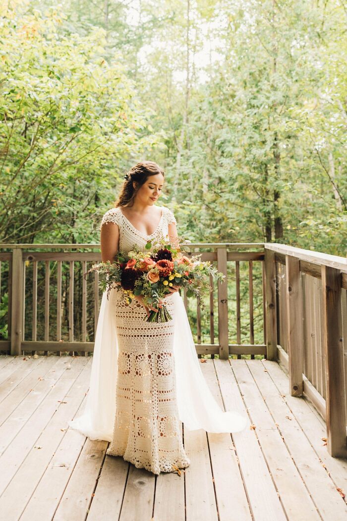 A beautiful bride in an awesome crocheted wedding gown on a wooden deck, holding a fall bouquet.