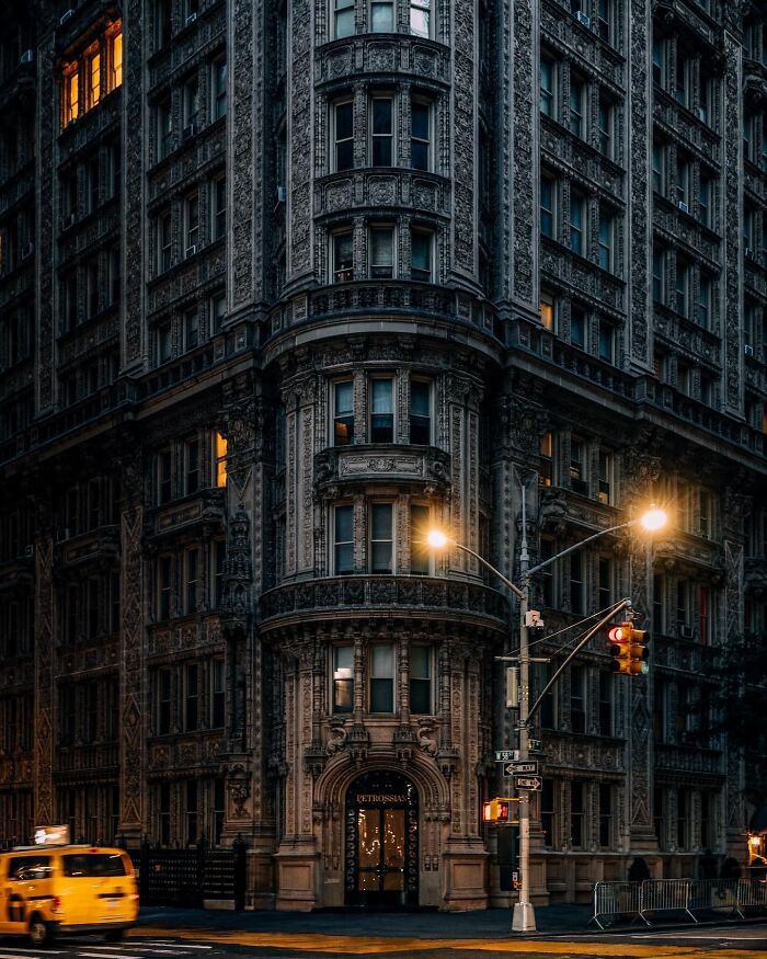 Stunning and beautiful architecture of an old, intricately detailed building at a street corner with glowing windows and streetlights.