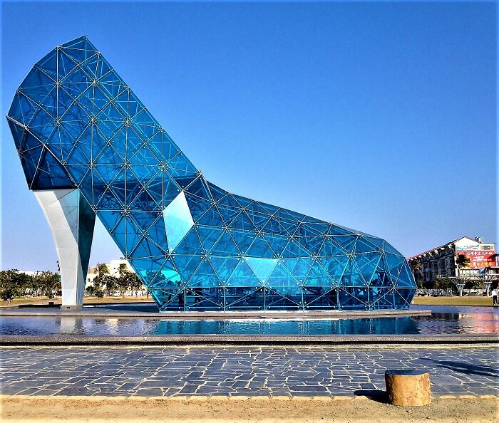 Unique glass high heel building sculpture reflecting in water under clear blue sky in unusual places worldwide.