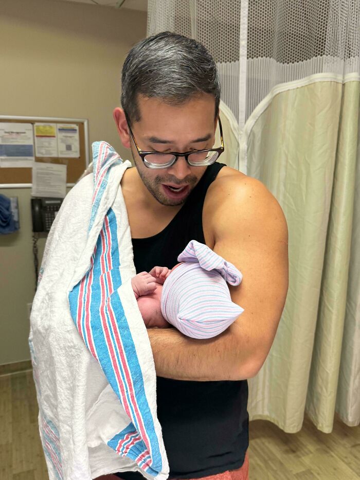 A wholesome and goofy photo of a great dad cradling his newborn baby in a hospital room.