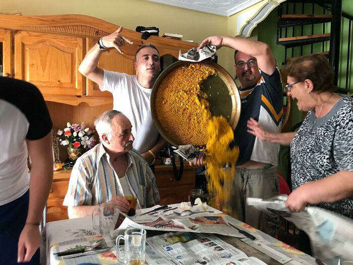Group of people at a table accidentally spilling a large pan of food, capturing an unexpected funny photo moment.