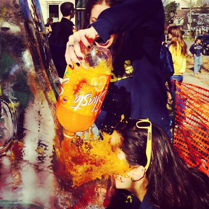 Person accidentally pouring orange soda on someone's face in a candid moment from people trying to take a photo.