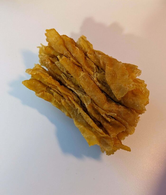 A giant absolute unit cornflake held on a white surface with a cereal box in the background.