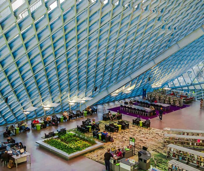 Modern and beautiful architecture of a large library interior with a glass ceiling, various seating areas, and people studying.