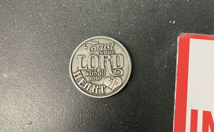 Silver coin with the inscription Trust in the Lord with all your heart on a black surface showing selfish and stupid behavior context