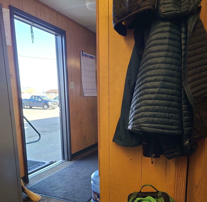 Interior of a small room with coats hanging, an open door showing a truck outside, illustrating selfish and stupid behavior.