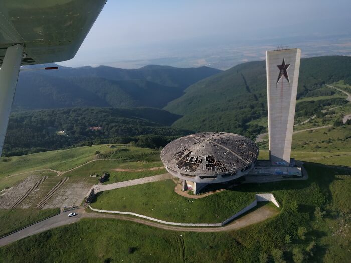 Aerial view of an unusual place with a unique circular building and tall monument in a mountainous area.