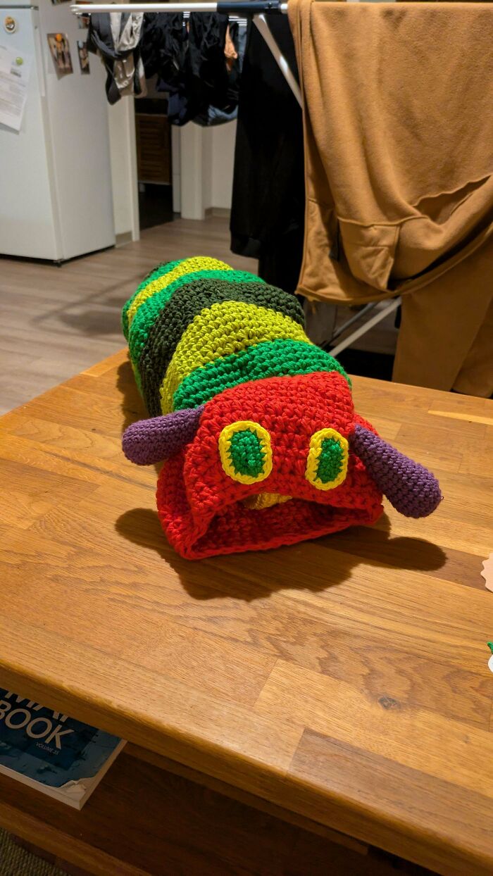 A colorful crocheted caterpillar, a fun example of crocheted something awesome, resting on a wooden table.