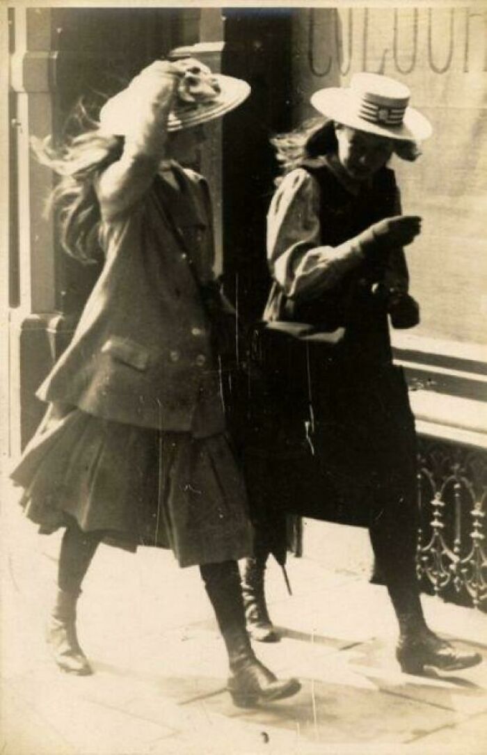 A candid old photo of two women walking on a street, both wearing hats and long skirts, revealing what the world looked like generations ago.