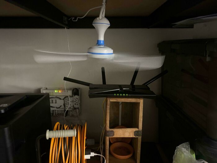Tech support workspace with a router on a wooden stand under a spinning ceiling fan and organized cables nearby.
