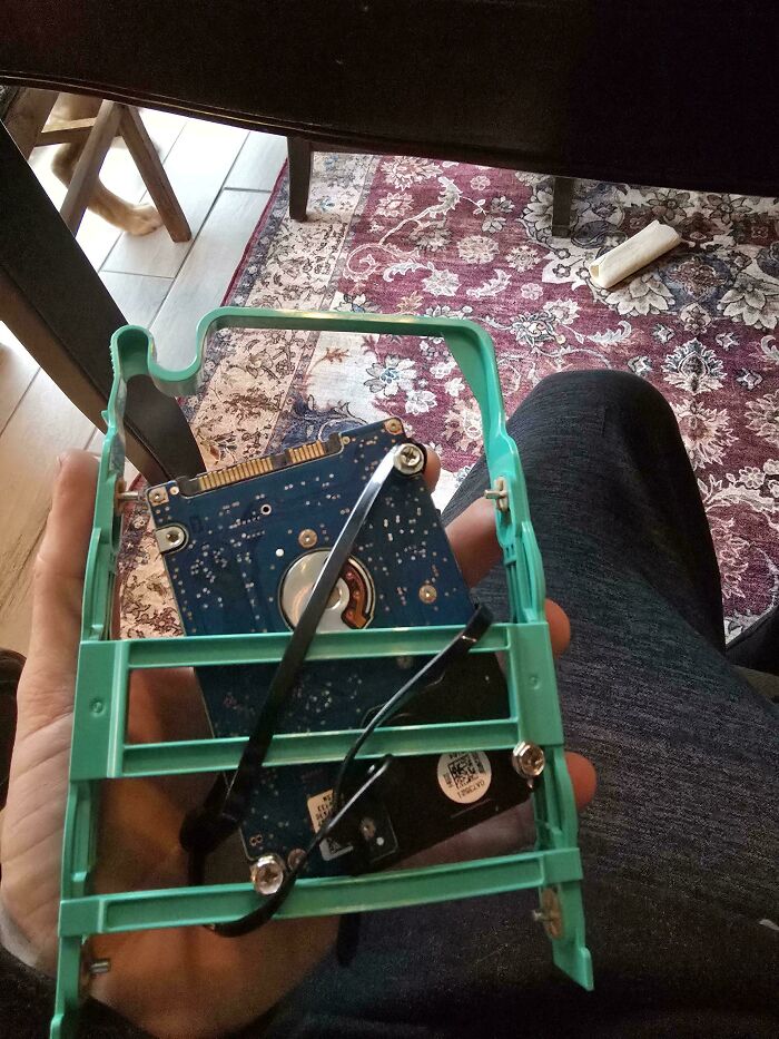 Tech support worker holding a damaged hard drive inside a green plastic frame, showing frustration with tech repair.