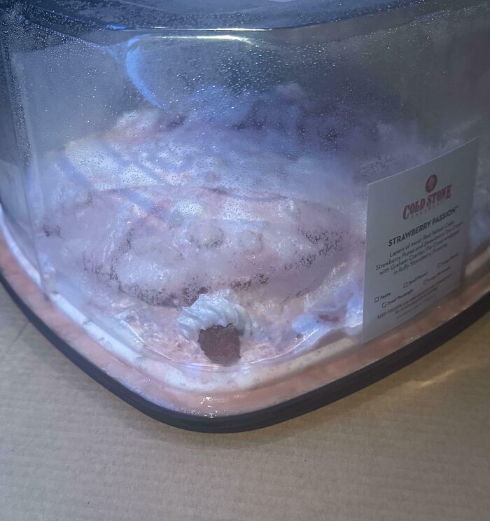 Partially melted Cold Stone Strawberry Passion ice cream in a fogged plastic container on a flat surface.