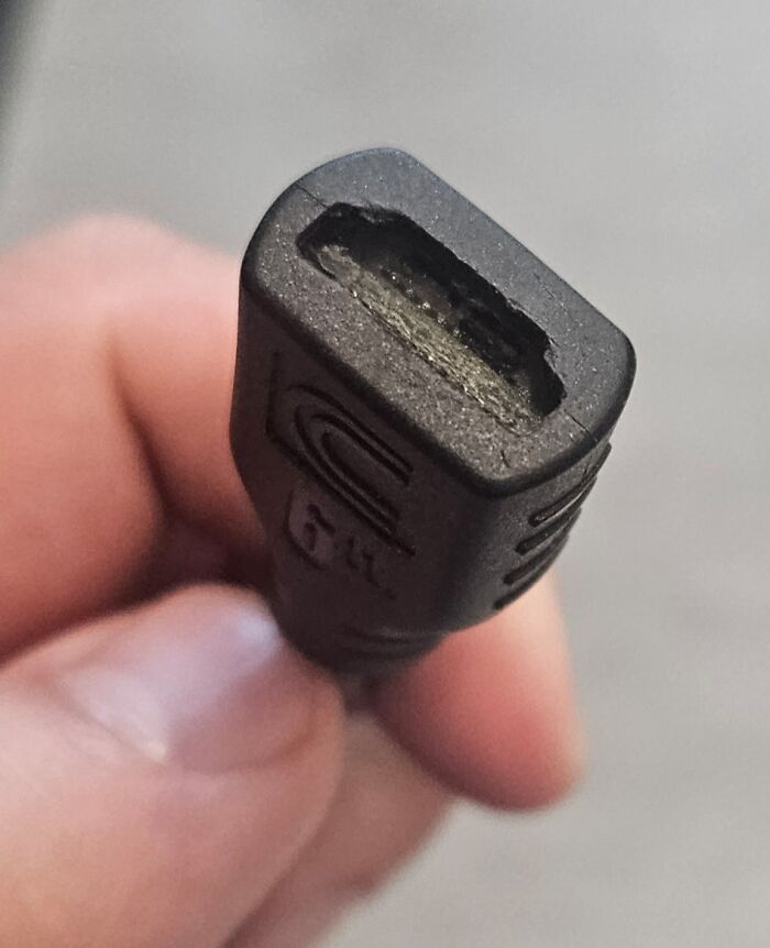 Close-up of damaged HDMI cable connector held by hand illustrating common tech support worker frustrations.