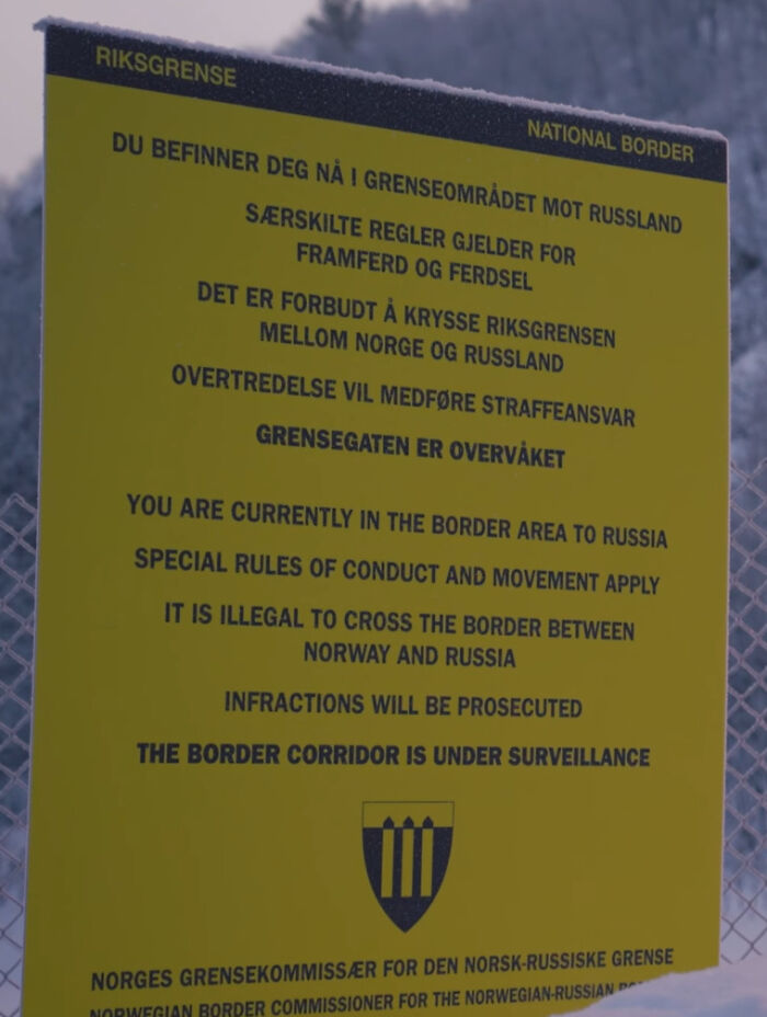 Yellow warning sign at the Norway-Russia border explaining illegal crossing and border corridor surveillance, a scary sign in the wild.
