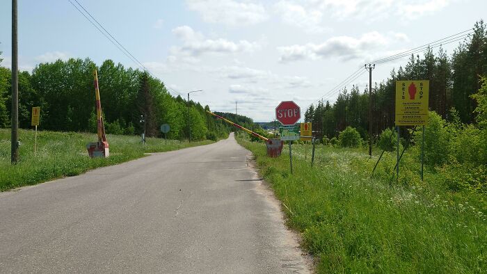 Rural road with multiple warning signs and a stop barrier suggesting hitchhikers may be escaping inmates in the area.