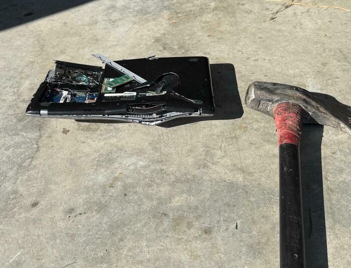 Hammer next to a heavily damaged laptop on concrete, illustrating boomers struggling with technology fails.